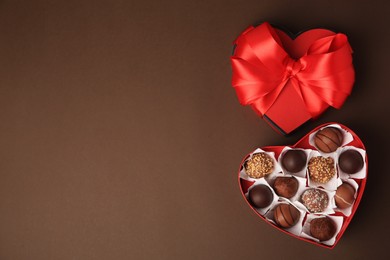 Heart shaped box with delicious chocolate candies on brown background, flat lay. Space for text