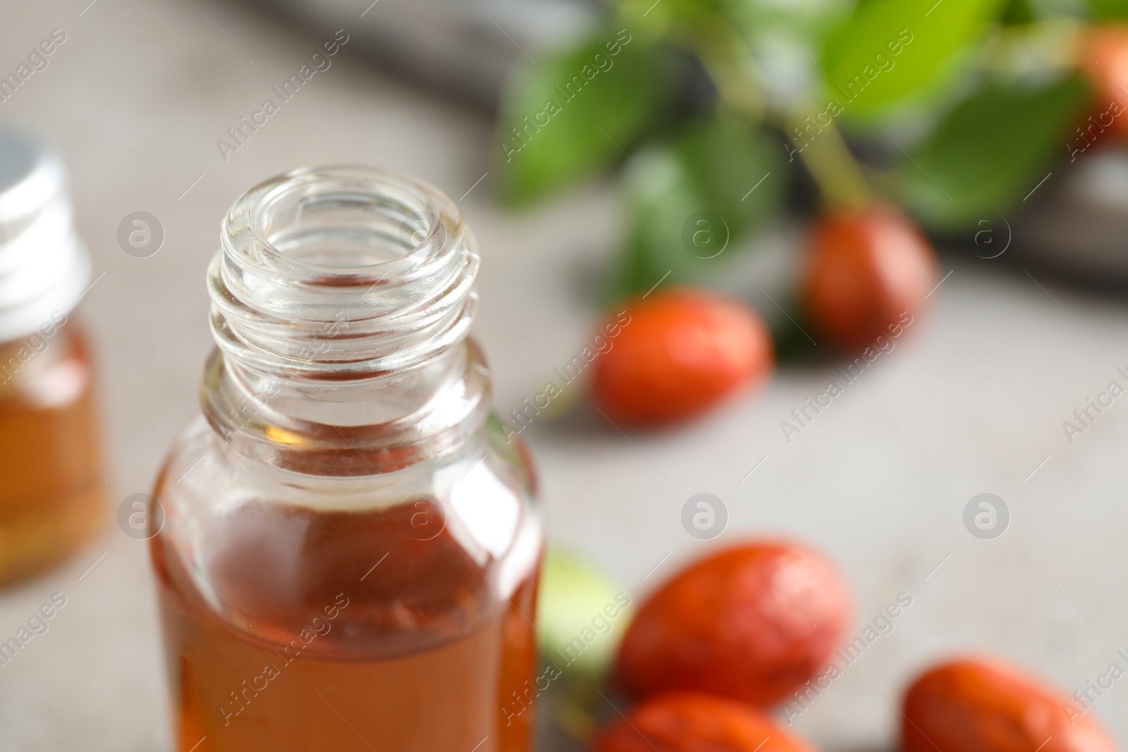 Photo of Glass bottle with jojoba oil and seeds on grey stone table, closeup. Space for text
