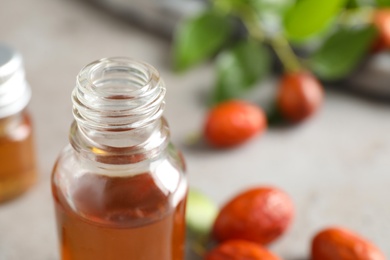 Photo of Glass bottle with jojoba oil and seeds on grey stone table, closeup. Space for text