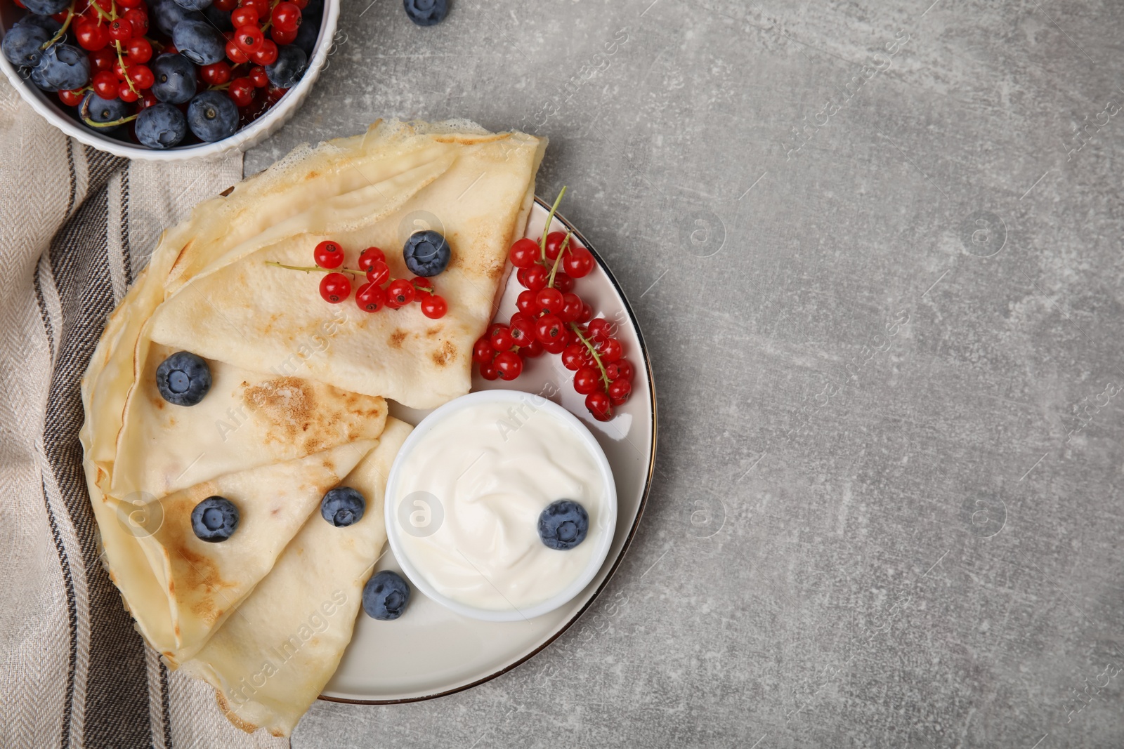 Photo of Delicious crepes with natural yogurt, blueberries and red currants on grey table, flat lay. Space for text