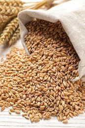 Photo of Sack with wheat grains on white wooden table, closeup