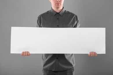 Photo of Man holding sheet of paper on grey background, closeup. Mockup for design