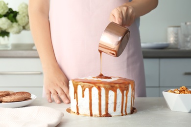 Photo of Young woman applying caramel sauce onto delicious homemade cake at table