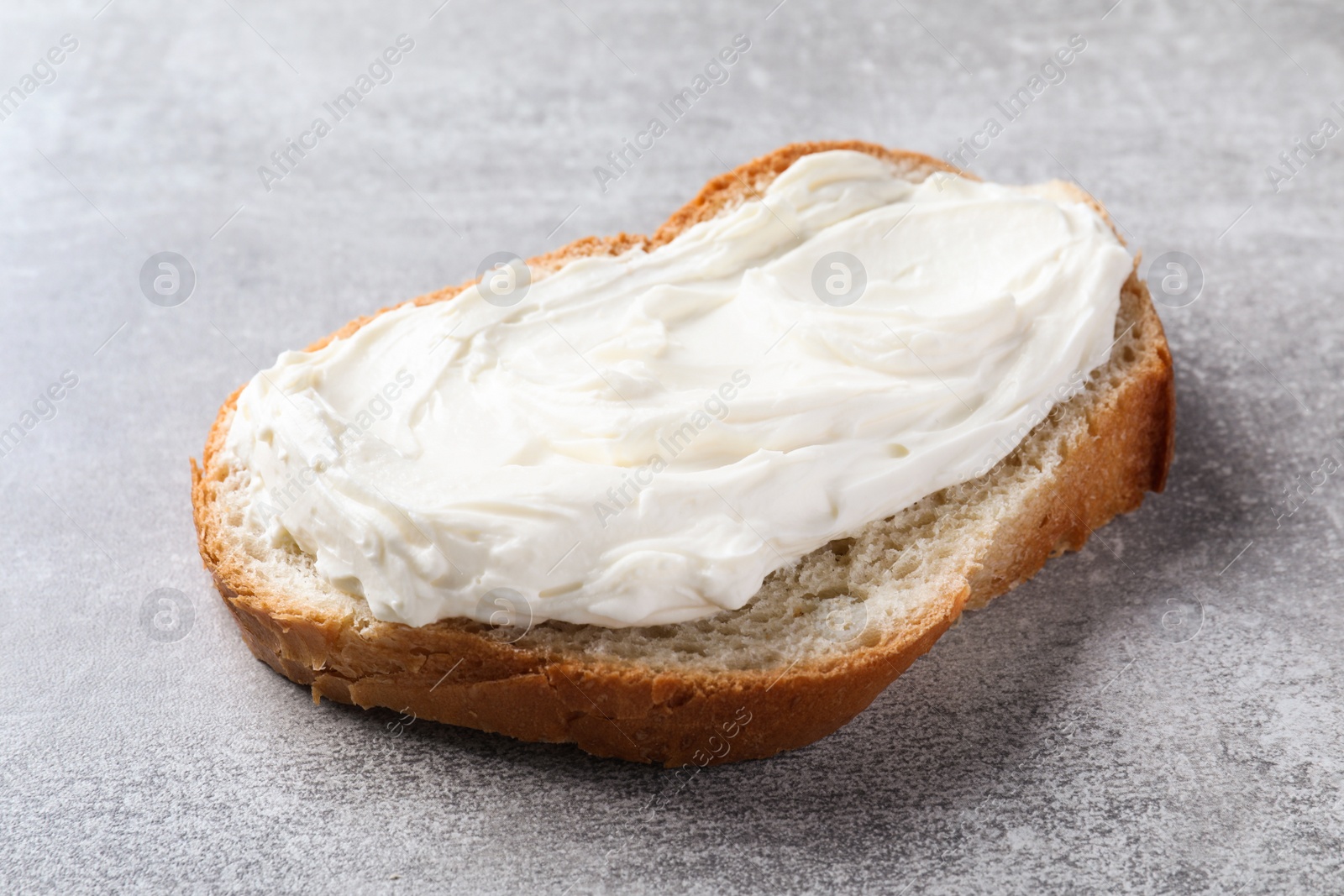 Photo of Slice of bread with tasty cream cheese on light grey table, closeup