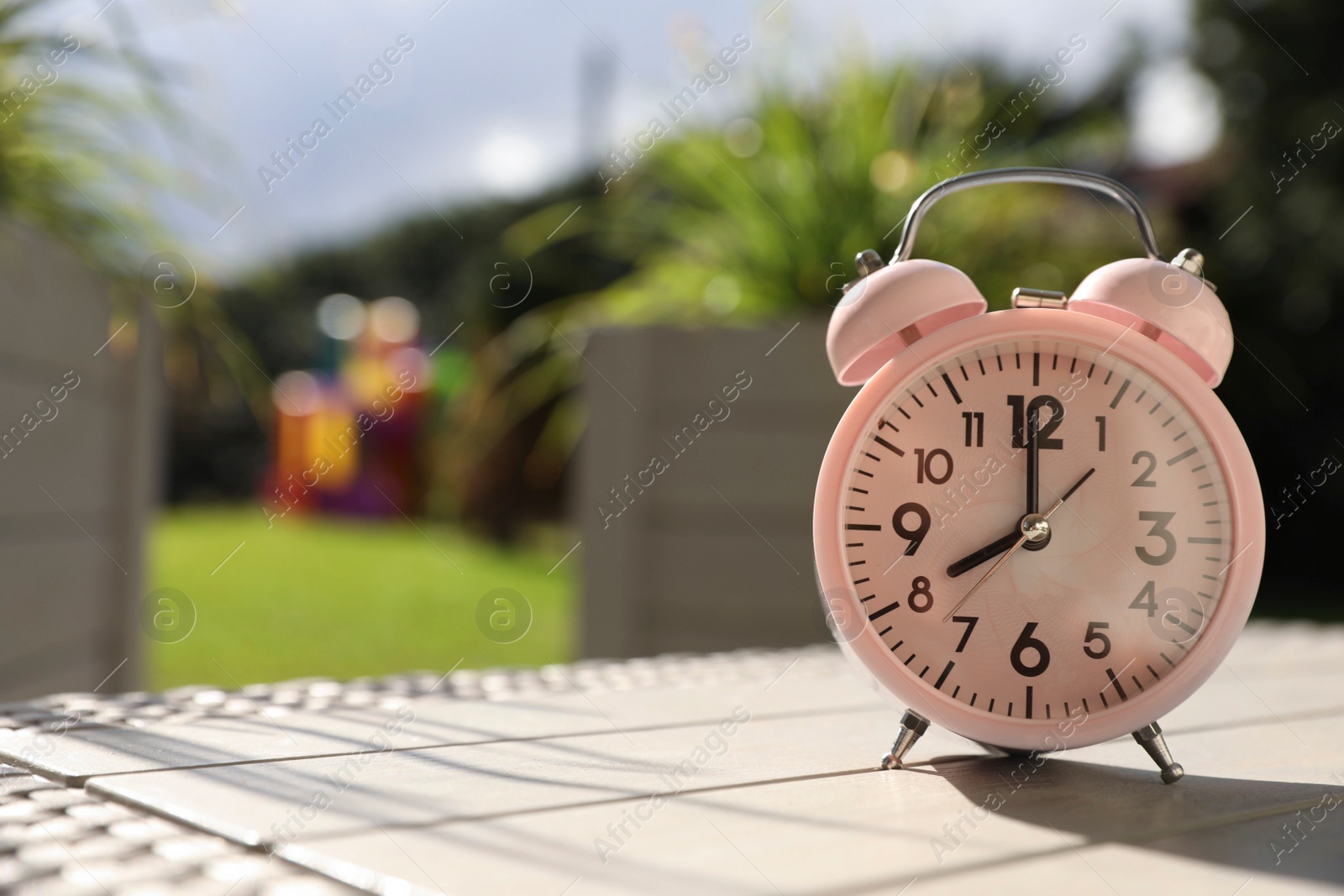 Photo of Pink alarm clock on table outdoors at sunny morning. Space for text