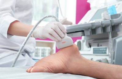 Photo of Doctor conducting ultrasound examination of patient's foot in clinic, closeup