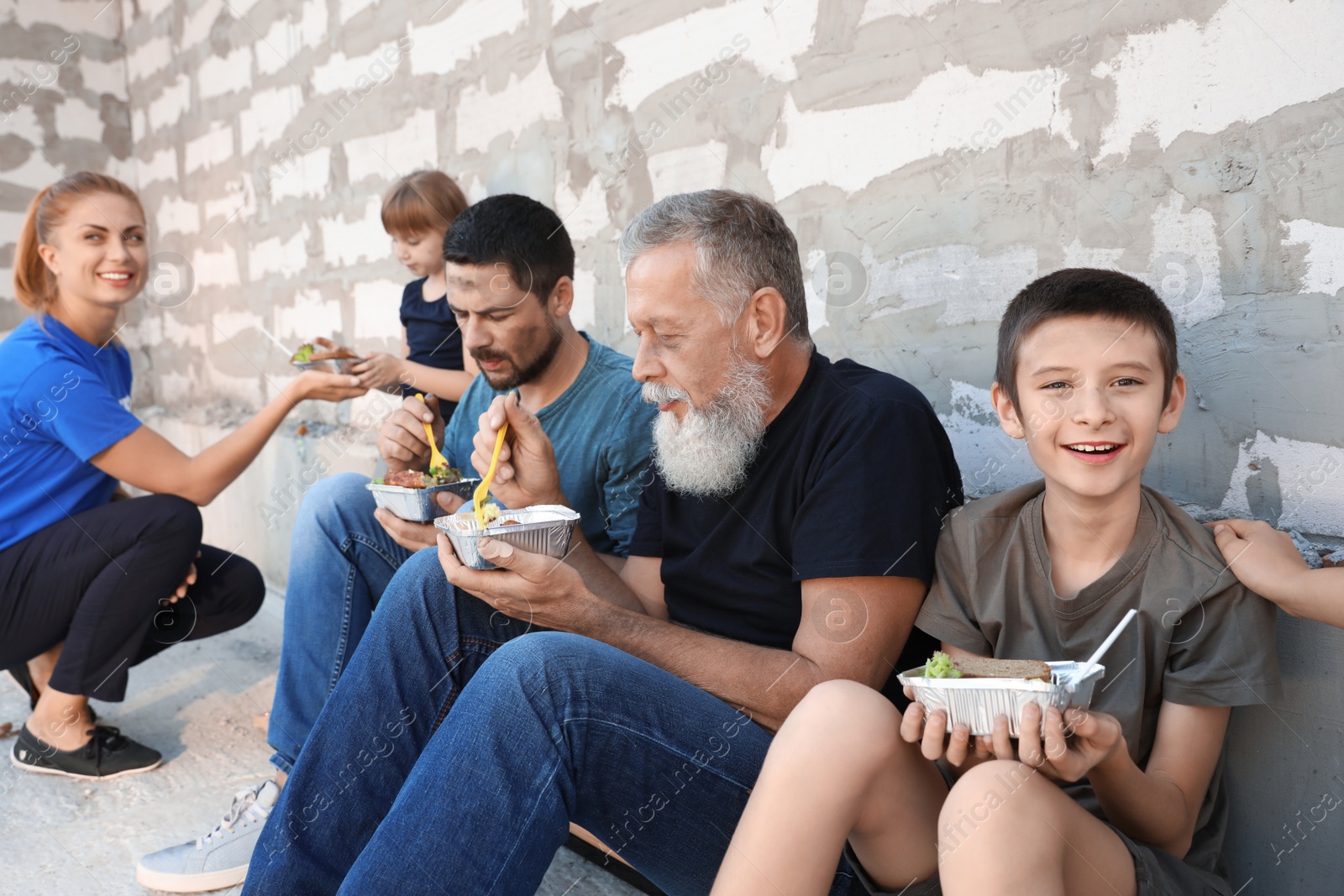 Photo of Poor people receiving food from volunteers near wall outdoors