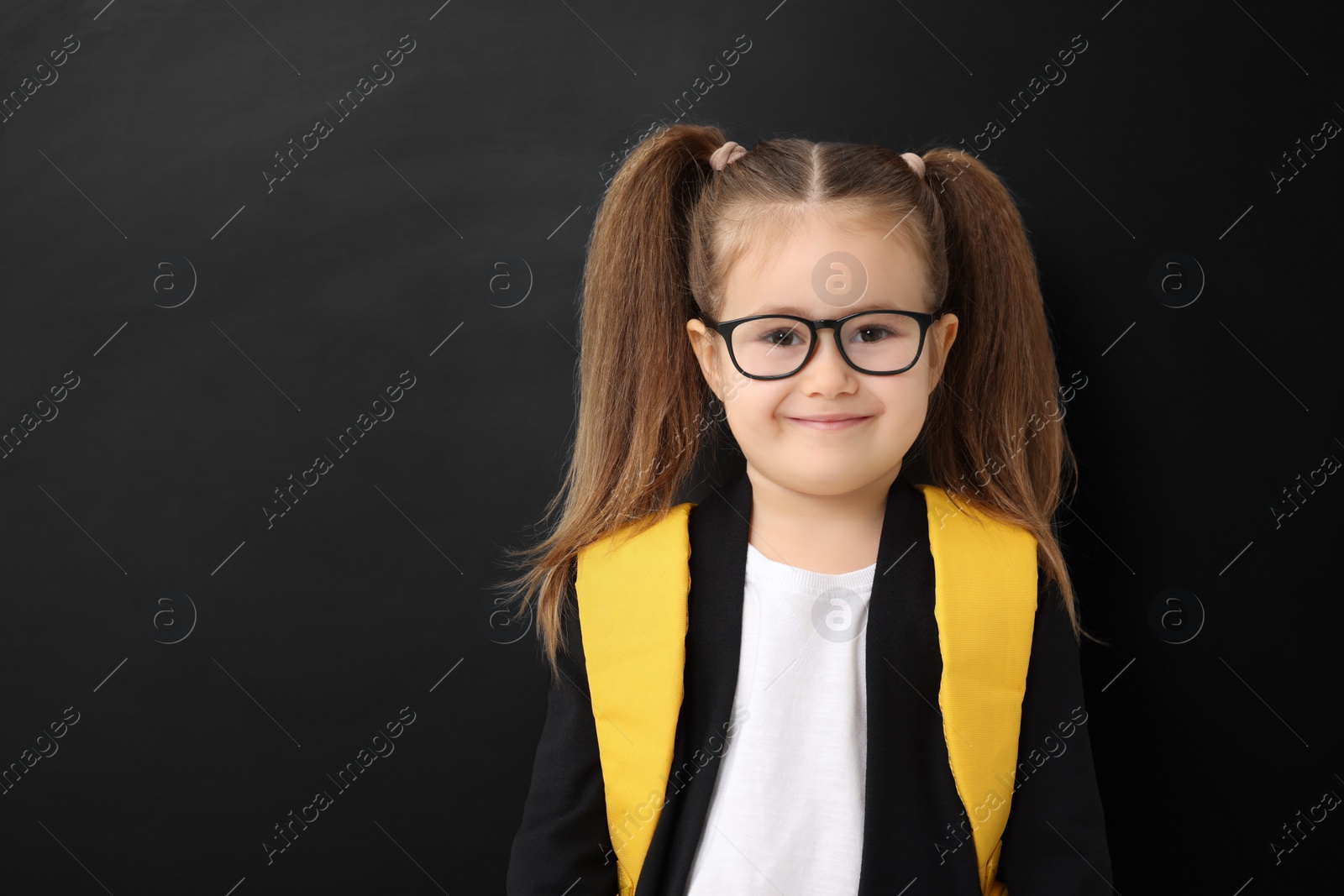 Photo of Happy little school child with backpack near chalkboard. Space for text