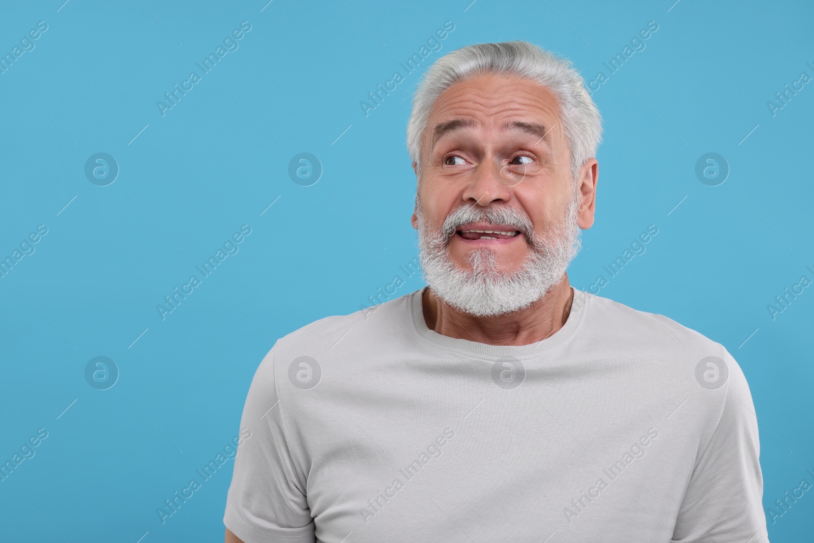 Photo of Portrait of embarrassed senior man on light blue background. Space for text