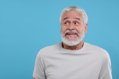 Portrait of embarrassed senior man on light blue background. Space for text