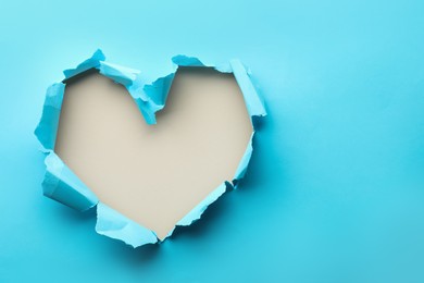 Photo of Torn heart shaped hole in light blue paper on white background, space for text