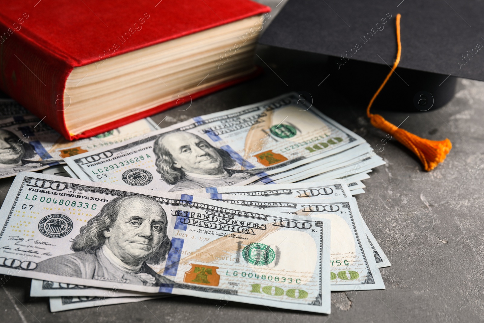 Photo of Dollars, student graduation hat and book on stone background. Tuition payments concept