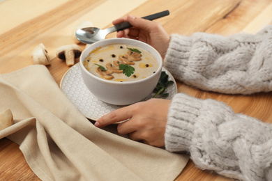 Photo of Woman with fresh mushroom soup  at wooden table, closeup