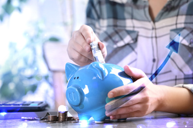 Image of Woman putting money into piggy bank at table, closeup