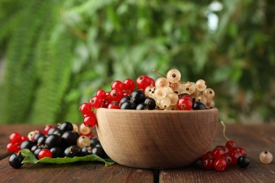 Different fresh ripe currants and green leaf on wooden table outdoors