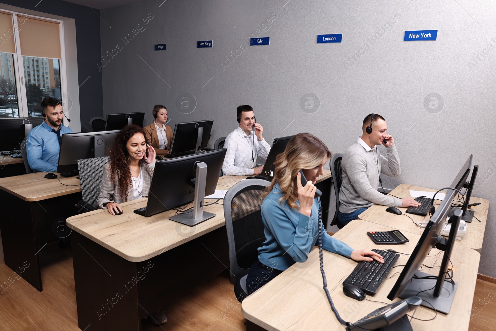 Photo of Young call center operator talking on phone and her colleagues working in modern office