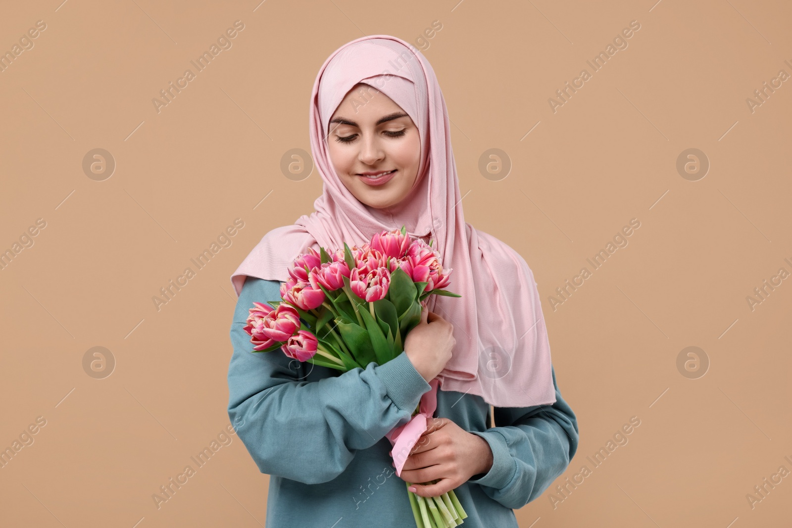 Photo of Happy woman in hijab with beautiful bouquet on beige background