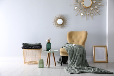 Photo of Soft knitted blanket on armchair in room. Home interior