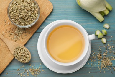 Photo of Fennel tea in cup, seeds and fresh vegetable on light blue wooden table, flat lay