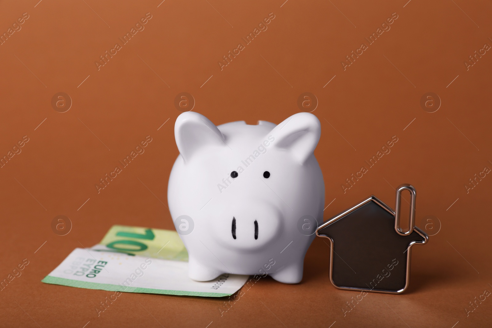 Photo of Ceramic piggy bank, euro banknote and key trinket on brown background. Financial savings