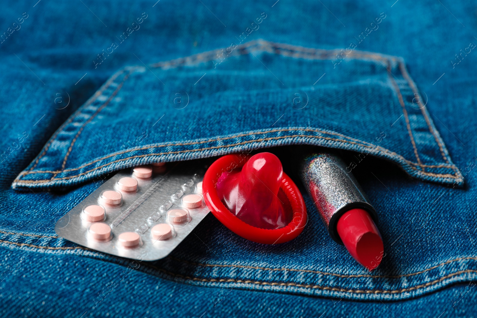 Photo of Red lipstick with condom and birth control pills in pocket of jeans, closeup. Safe sex concept