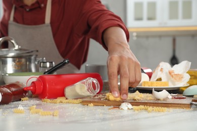 Photo of Man taking cheese from table in messy kitchen, closeup. Many dirty dishware, utensils and food leftovers on table