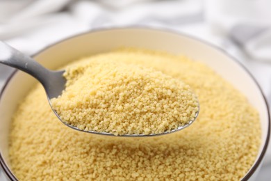 Photo of Taking raw couscous with spoon from bowl, closeup