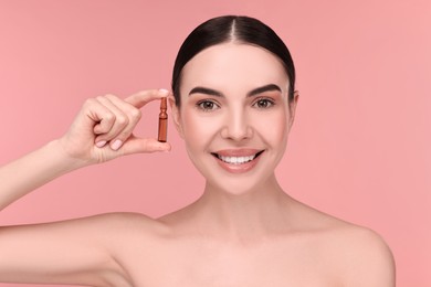 Beautiful young woman holding skincare ampoule on pink background