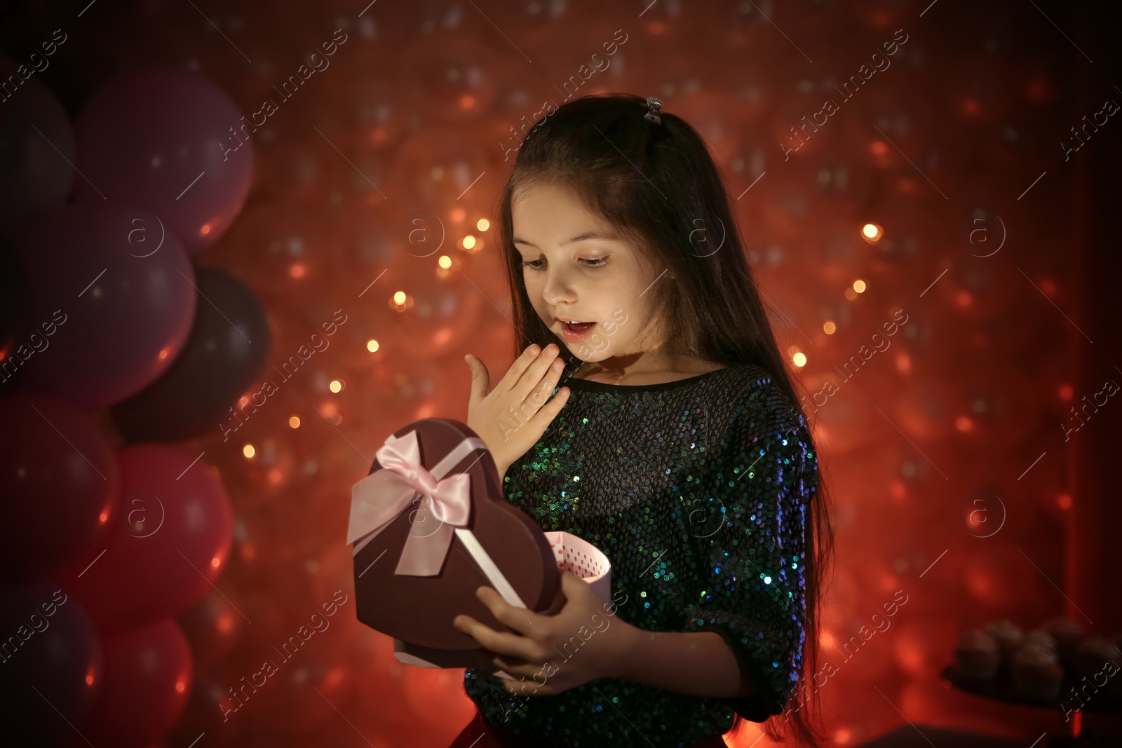 Photo of Happy little girl with gift in beautifully decorated room at home. Birthday celebration