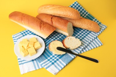 Photo of Whole and cut baguettes with fresh butter on yellow background, above view