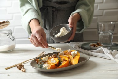 Photo of Woman putting cheese on baked pumpkin slices at table, closeup