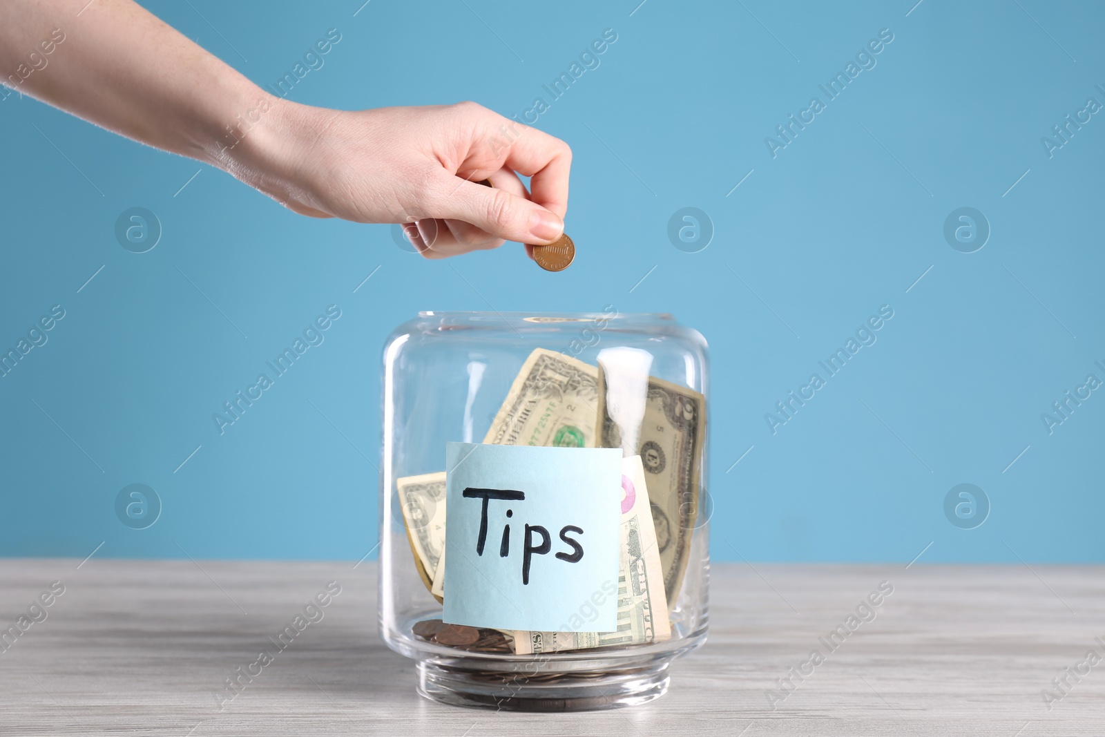 Photo of Woman putting tips into glass vase on wooden table, closeup
