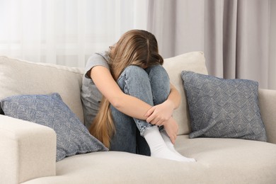 Depressed teenage girl sitting on sofa at home