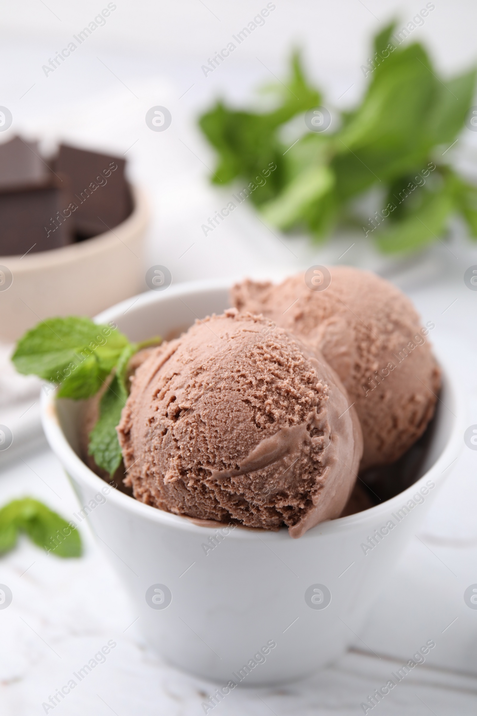 Photo of Bowl with tasty chocolate ice cream and mint leaves on white table, closeup