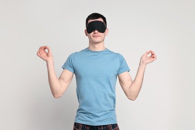 Photo of Man in pyjama and sleep mask meditating on light grey background