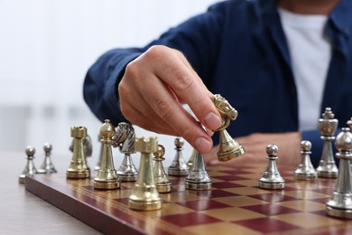 Man moving knight on chessboard at table indoors, closeup