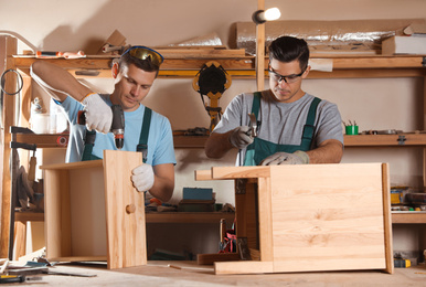Photo of Professional carpenters assembling wooden cabinet in workshop