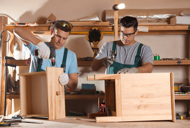 Professional carpenters assembling wooden cabinet in workshop