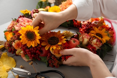 Florist making beautiful autumnal wreath with flowers and fruits at light grey table, closeup