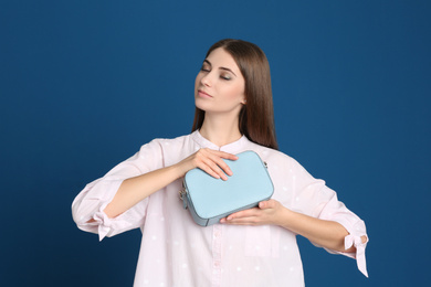 Beautiful young woman with stylish bag on blue background