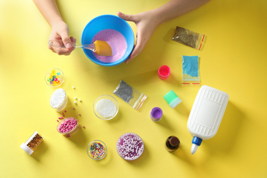 Photo of Little girl making slime toy on yellow background, top view