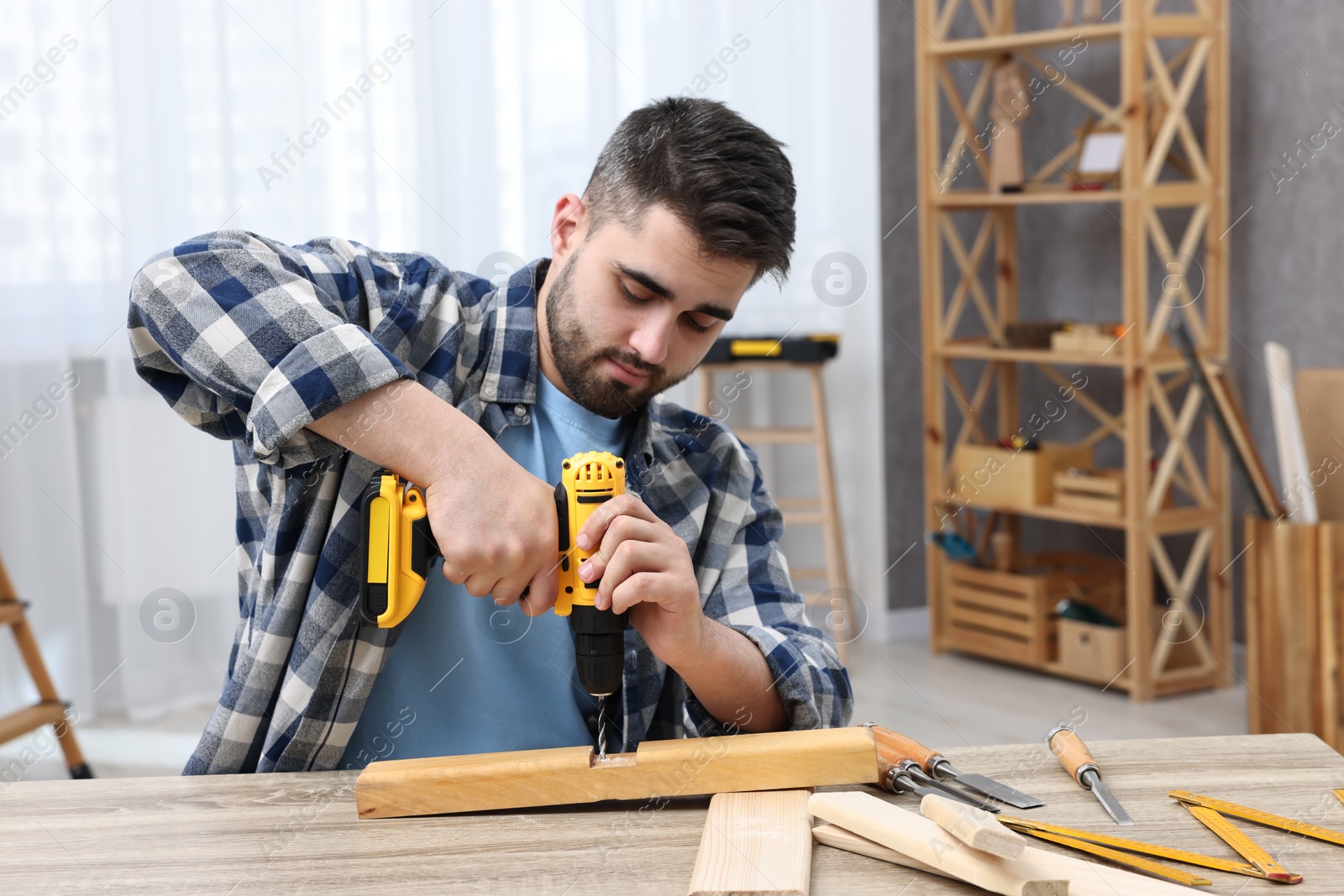 Photo of Young handyman working with electric drill at table in workshop