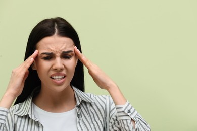 Woman suffering from migraine on light green background, space for text