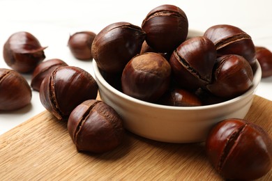 Photo of Bowl with roasted edible sweet chestnuts on white table, closeup