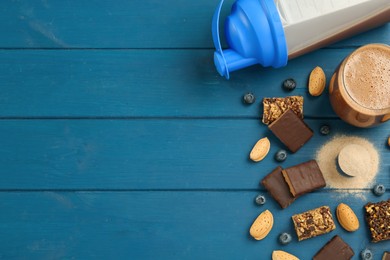 Different energy bars, nuts, blueberries, protein cocktail and powder on blue wooden table, flat lay. Space for text