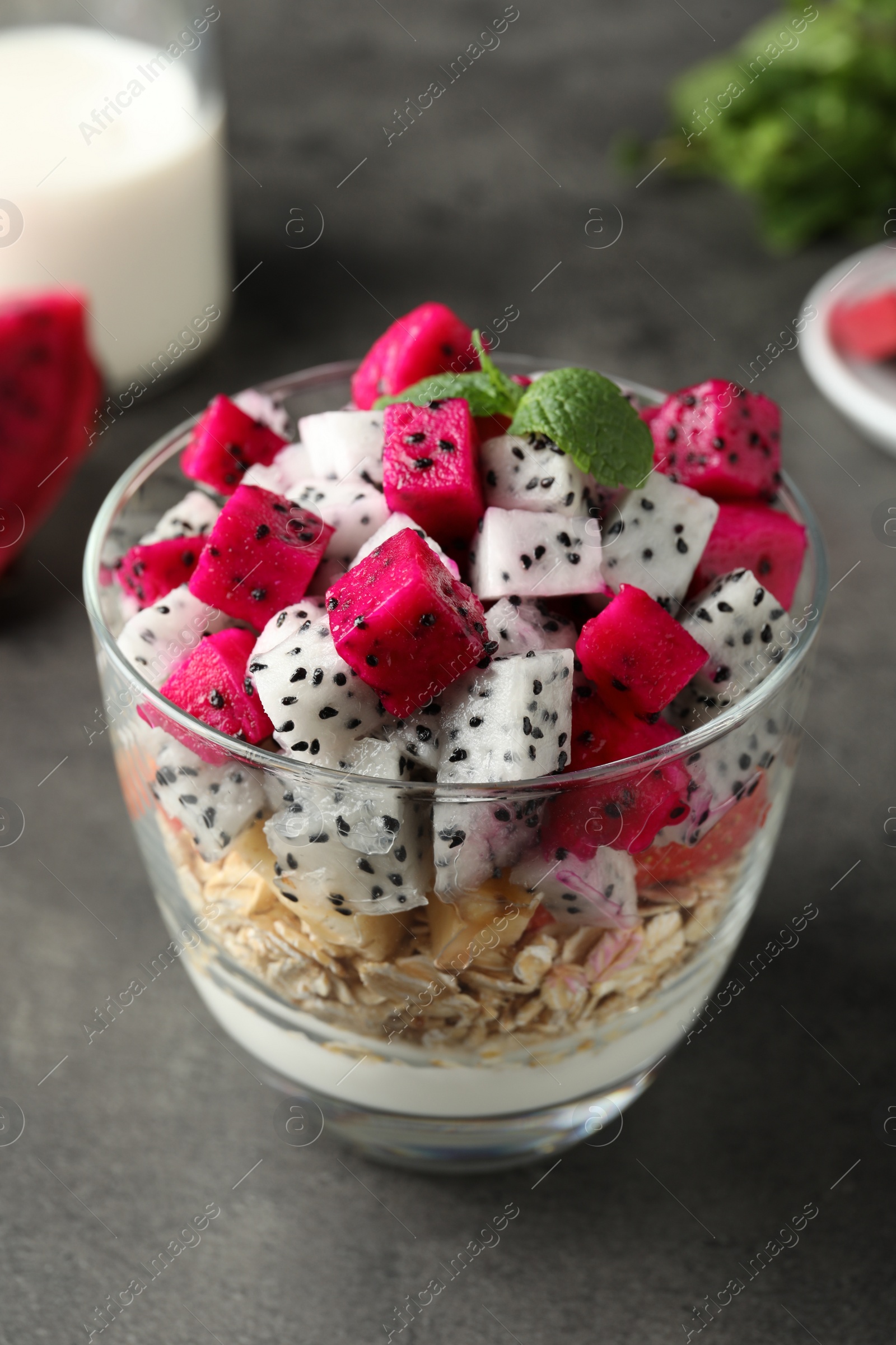 Photo of Glass of granola with different pitahayas, yogurt and mint on grey table