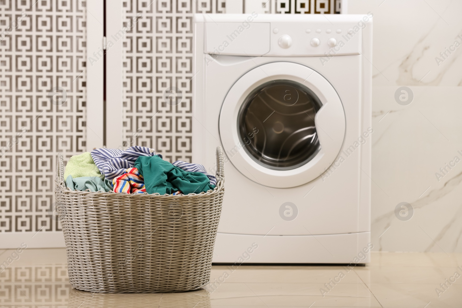 Photo of Wicker basket with dirty clothes on floor in laundry room