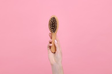 Woman holding brush with lost hair on pink background, closeup. Alopecia problem