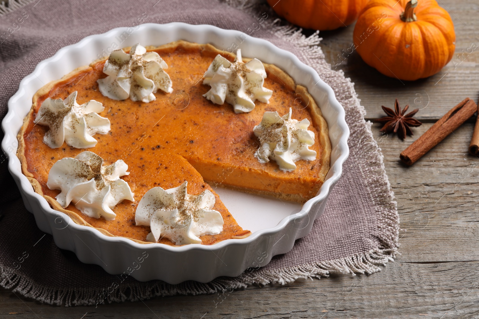 Photo of Delicious pie with pumpkins, whipped cream and spices on wooden table