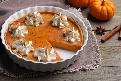 Delicious pie with pumpkins, whipped cream and spices on wooden table